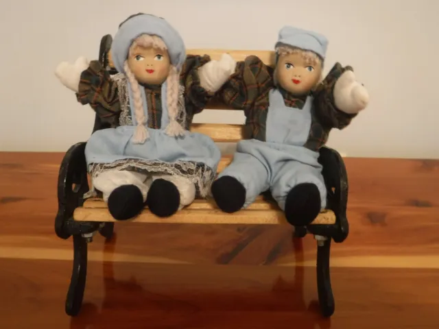 Vintage Boy and Girl porcelain dolls sitting on a wooden and iron bench