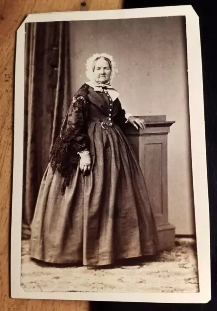 standing old woman in mature skirt with hood - backdrop - circa 1860s CDV