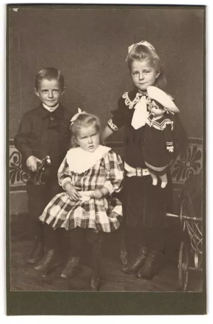 Fotografie drei niedliche Kinder mit Puppe in der Hand und Knabe mit Spielzeug