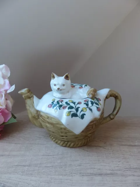 Théière chat en porcelaine allongé sur une couverture dans un panier, cat teapot