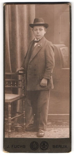 Fotografie J. Fuchs, Berlin, Portrait junger Mann im Anzug mit Hut an Stuhl gel