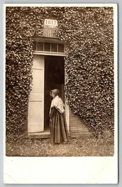 Postcard RPPC Young Amish Woman Scowling in Front of Ivy Covered Wall & Door
