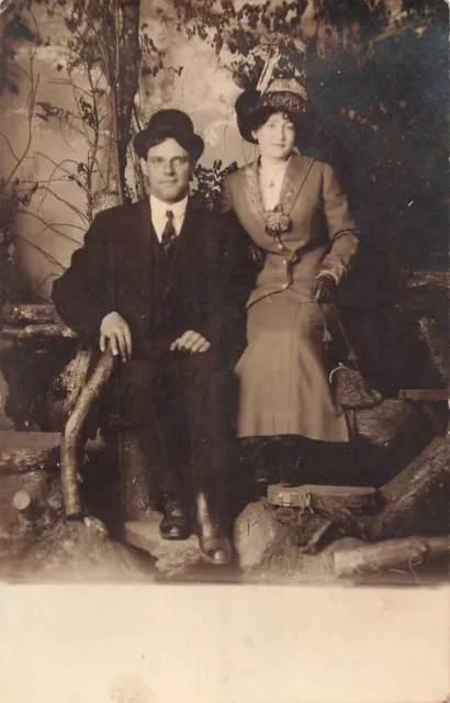 YOUNG COUPLE SITTING ON LOGS-PERIOD ATTIRE~1910s REAL PHOTO POSTCARD