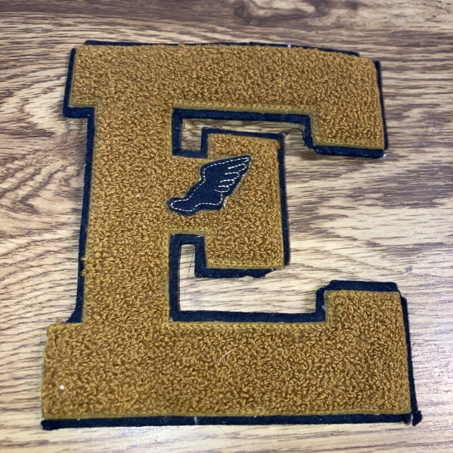 Vintage Varsity Letter: E golden brownish with Black outline, Winged foot logo