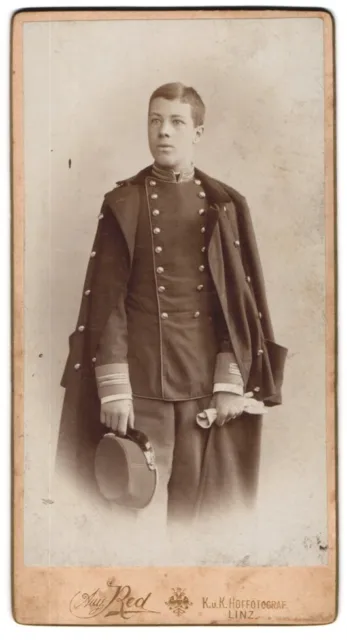 Fotografie Aug. Red, Linz, Portrait Knabe in Uniform als K.u.K. Kadett mit Mant