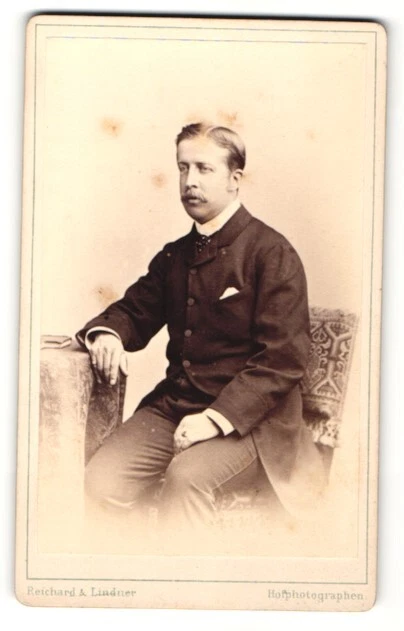 Fotografie Reichard & Lindner, Berlin, Portrait älterer Herr im Mantel am Tisch