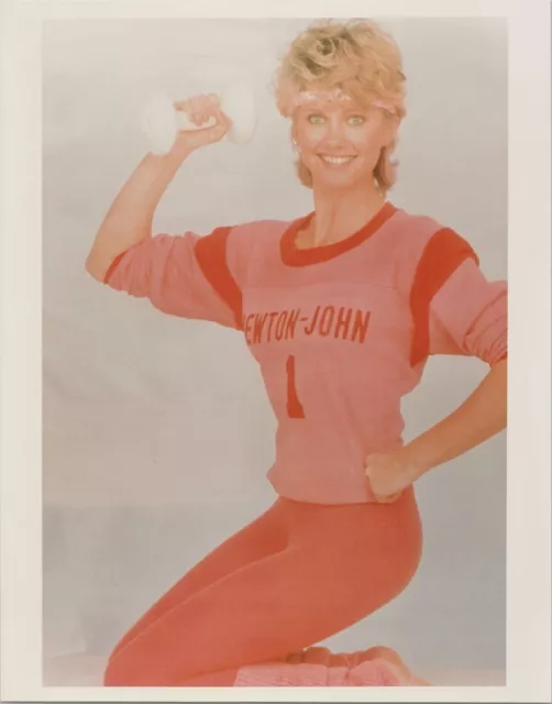 Olivia Newton-John poses smiling in orange work-out outfit holding dumbell 8x10