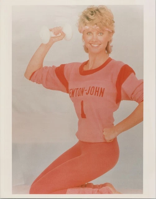 Olivia Newton-John poses smiling in orange work-out outfit holding dumbell 8x10