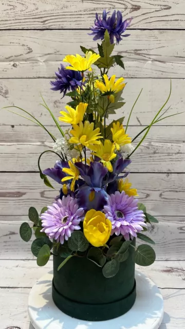A beautiful purple & yellow artificial flower display in a green suede hatbox