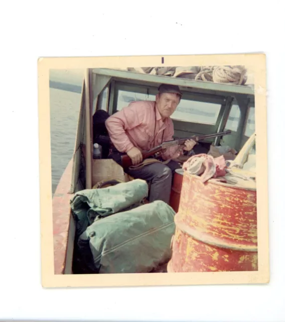 Man in fishing boat with gun rifle    Vintage color snapshot photo.