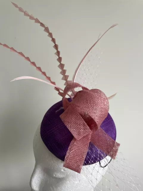 Purple fascinator with round base and pink loops, netting and feathers.