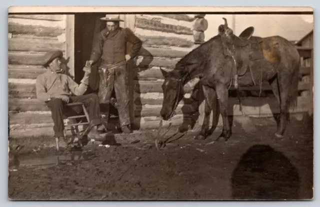 RPPC Cowboy @ Log Cabin Door w/Pistol Hands Gadget to Another~Sad Horse w/Saddle