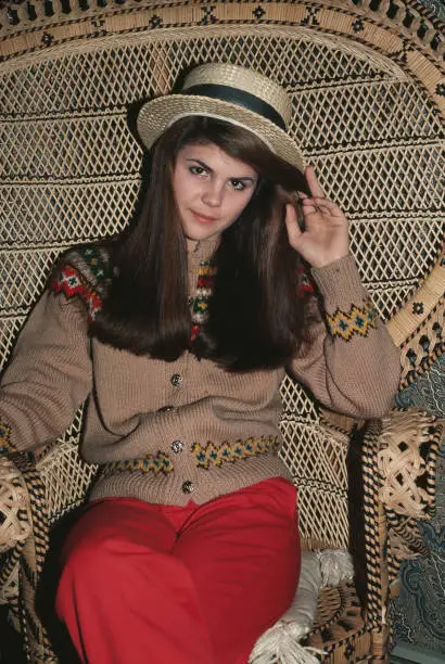 Lori Loughlin wearing boater straw hat sits on a peacock wicker ch- Old Photo